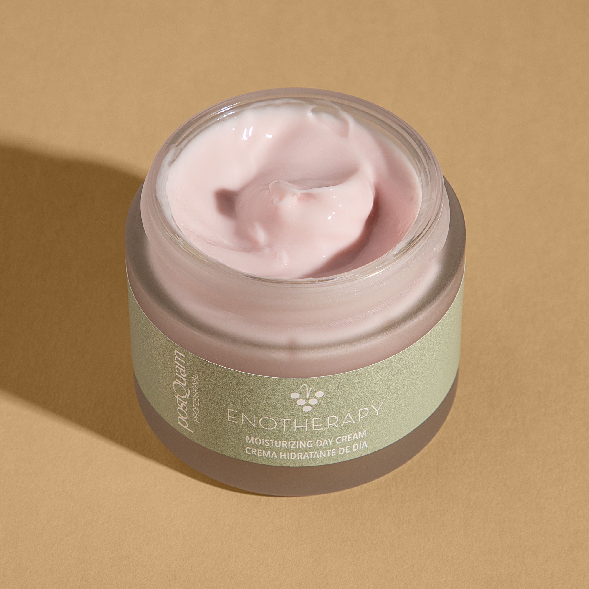 Geöffneter Creme-Tiegel. Rosa Creme sichtbar. Aufschrift: PostQuam, Enotherapy, Moisturizing Day Cream. Grüner Aufkleber.