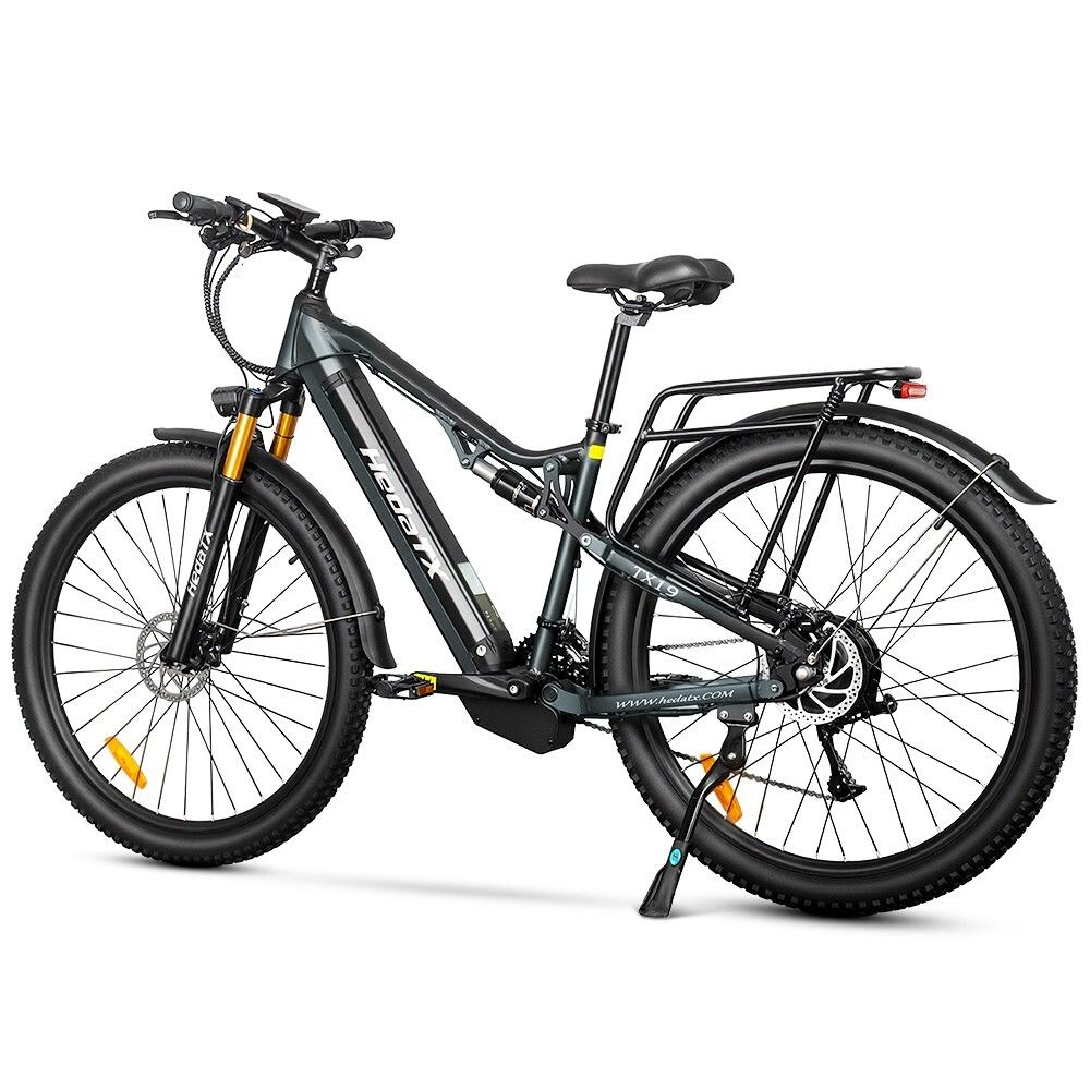 Graues E-Bike HedaTX TX19. Schwarze Reifen, Gepäckträger, Federung. Gelbe Gabel. 27 Gänge. Aufschrift HedaTX.