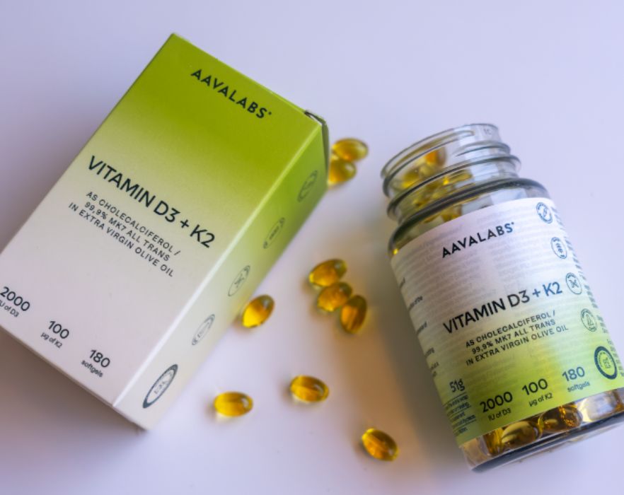 Aavalabs Vitamin D3+K2 Softgels neben einer geöffneten Flasche und einer Schachtel, einige Softgels verstreut.
