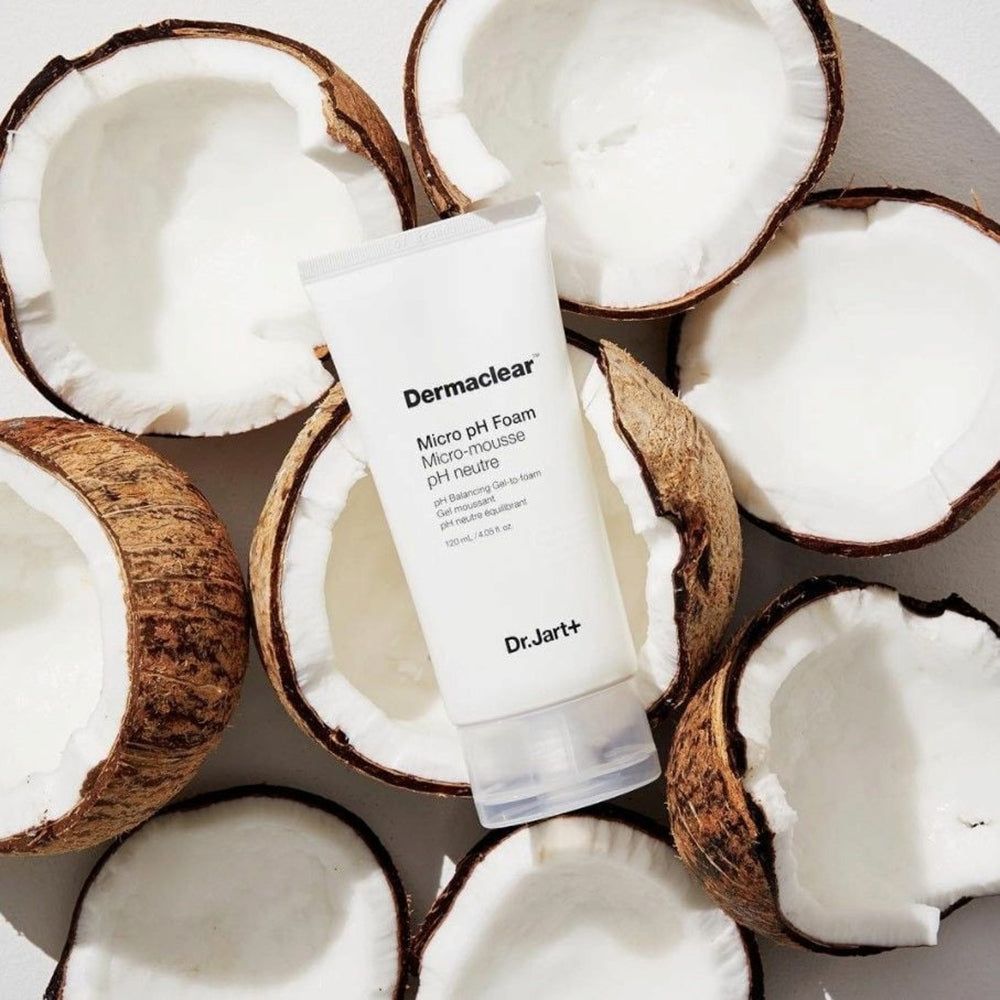 Weiße Tube mit Produkttext auf Kokosnüssen. Aufschrift: Dermaclear Micro pH Foam, Dr.Jart+. Umgeben von Kokosnussschalen.