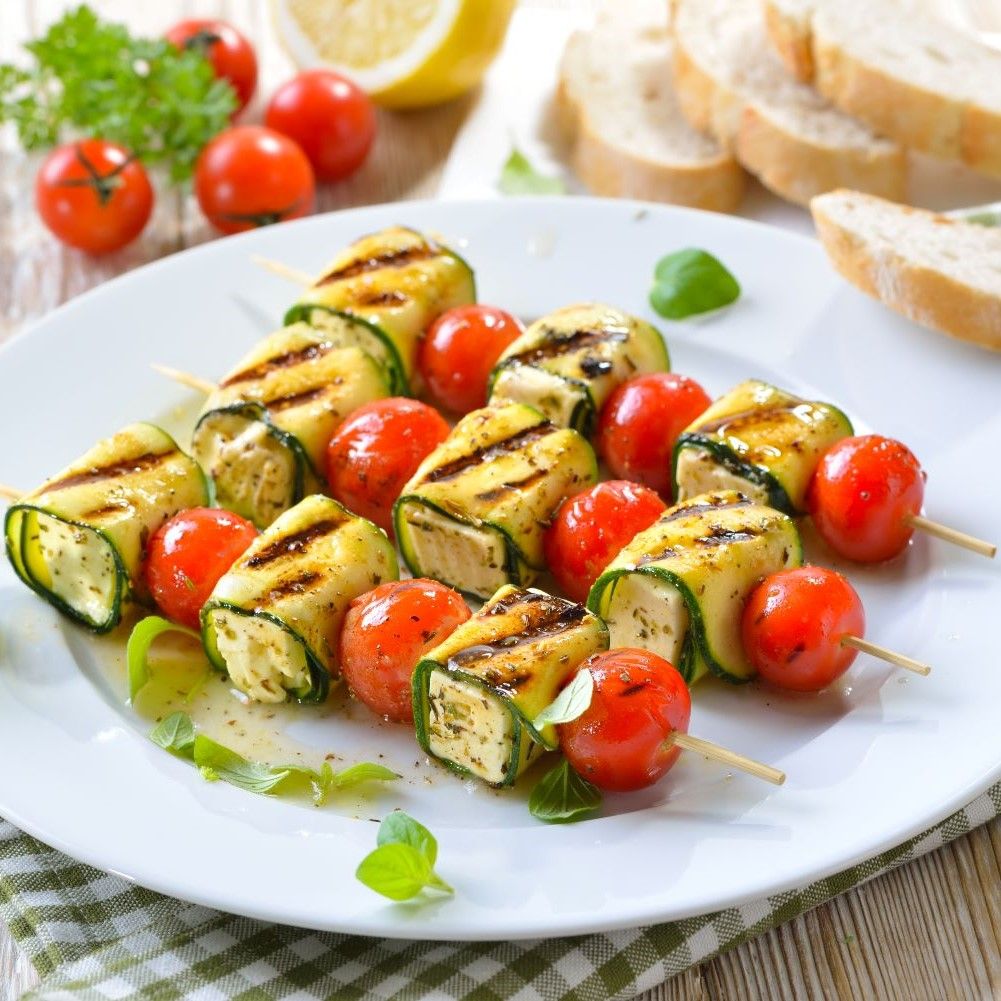 Spieße mit gegrillten Zucchiniröllchen und Kirschtomaten. Auf einem Teller angerichtet, mit Brot.