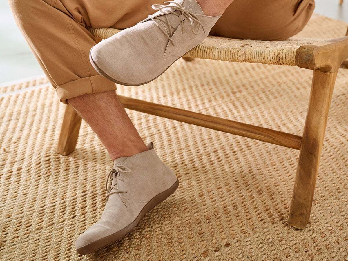 Mann sitzt auf einem Stuhl und trägt hellbraune Stiefeletten. Schnürung, flache Sohle.