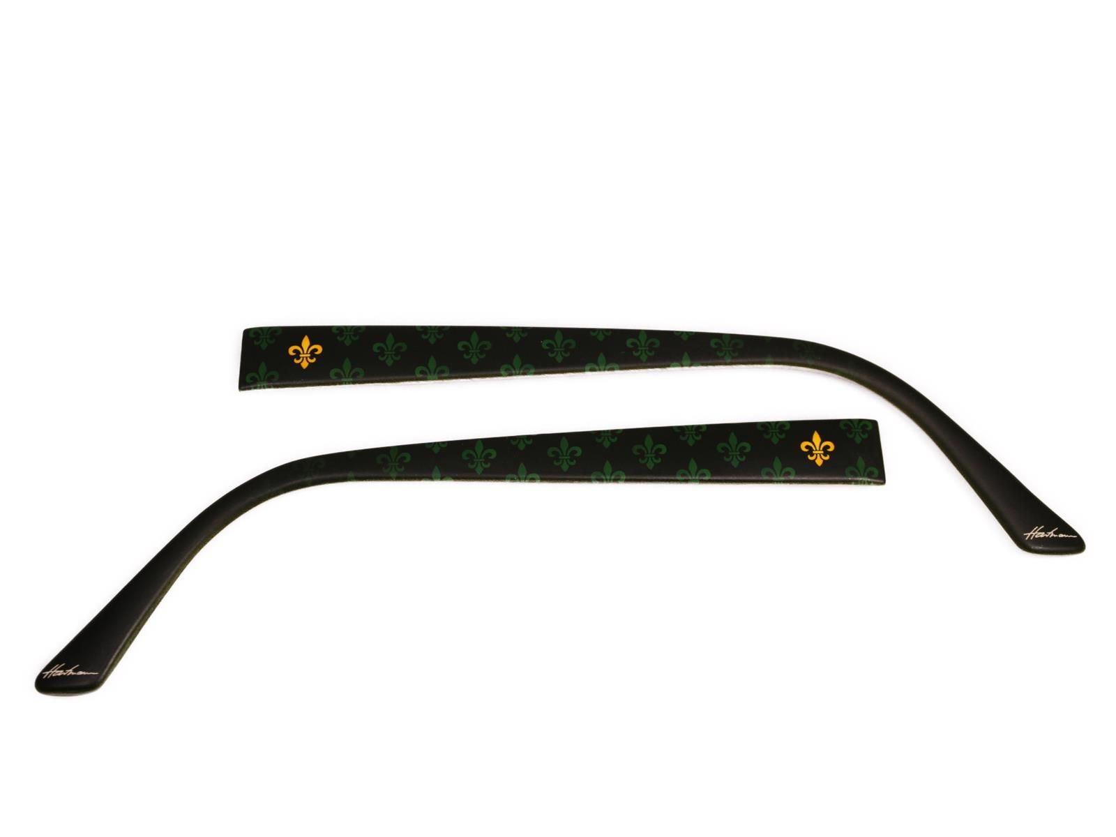 Zwei schwarze Brillenbügel mit grünem Muster und goldenen Lilien. Schwarze Enden mit Schriftzug.