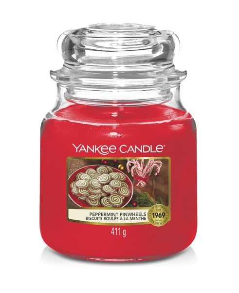 Rote Duftkerze mit Glasdeckel. Aufkleber mit Keksen, Schriftzug "Peppermint Pinwheels" und "Yankee Candle". Gewicht: 411 g.