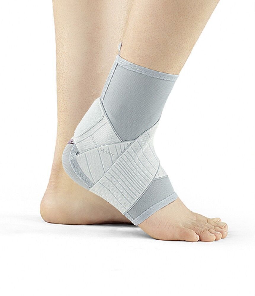 Knöchelbandage, grau-weiß. Bandage am Fuß getragen. Klettverschlüsse und Verstärkungen sichtbar. Produkt am Fuß einer Person.