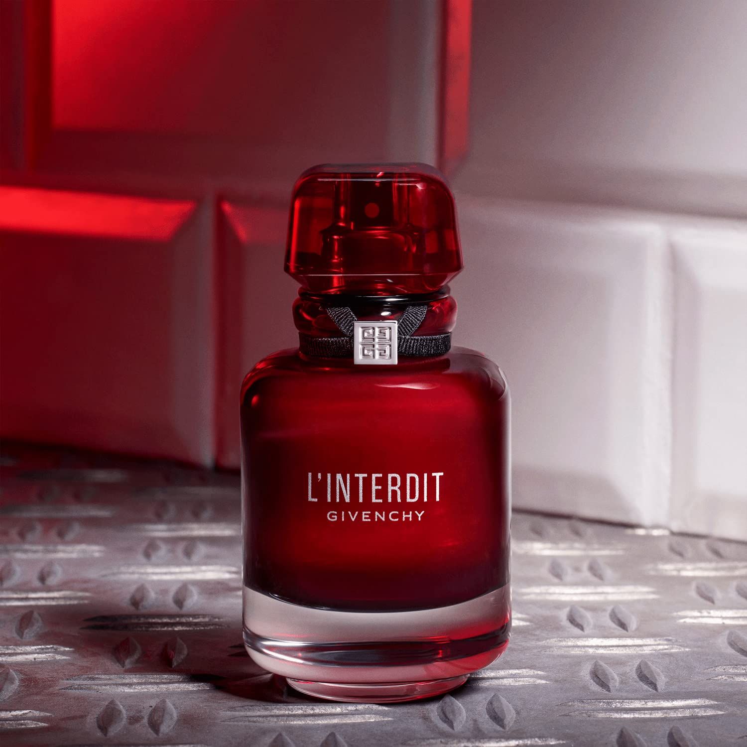 Rote Flasche mit schwarzem Band und silbernem Verschluss. Hintergrund: weiß-graue Fliesen und metallische Oberfläche.