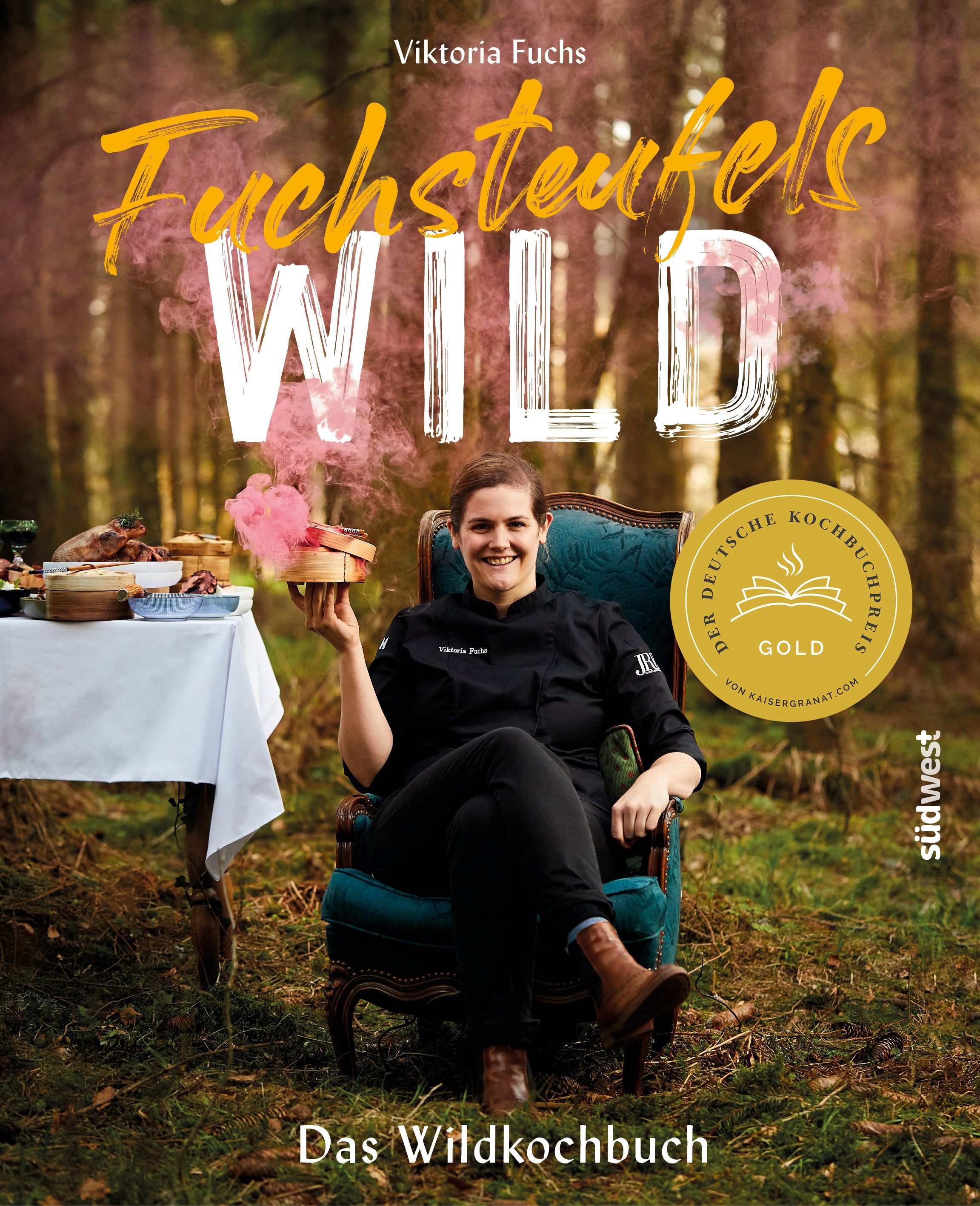 Buchcover mit Titel "Fuchsteufelswild". Frau sitzt in Sessel, hält Geschenk. Goldener Kochbuchpreis. Waldhintergrund.