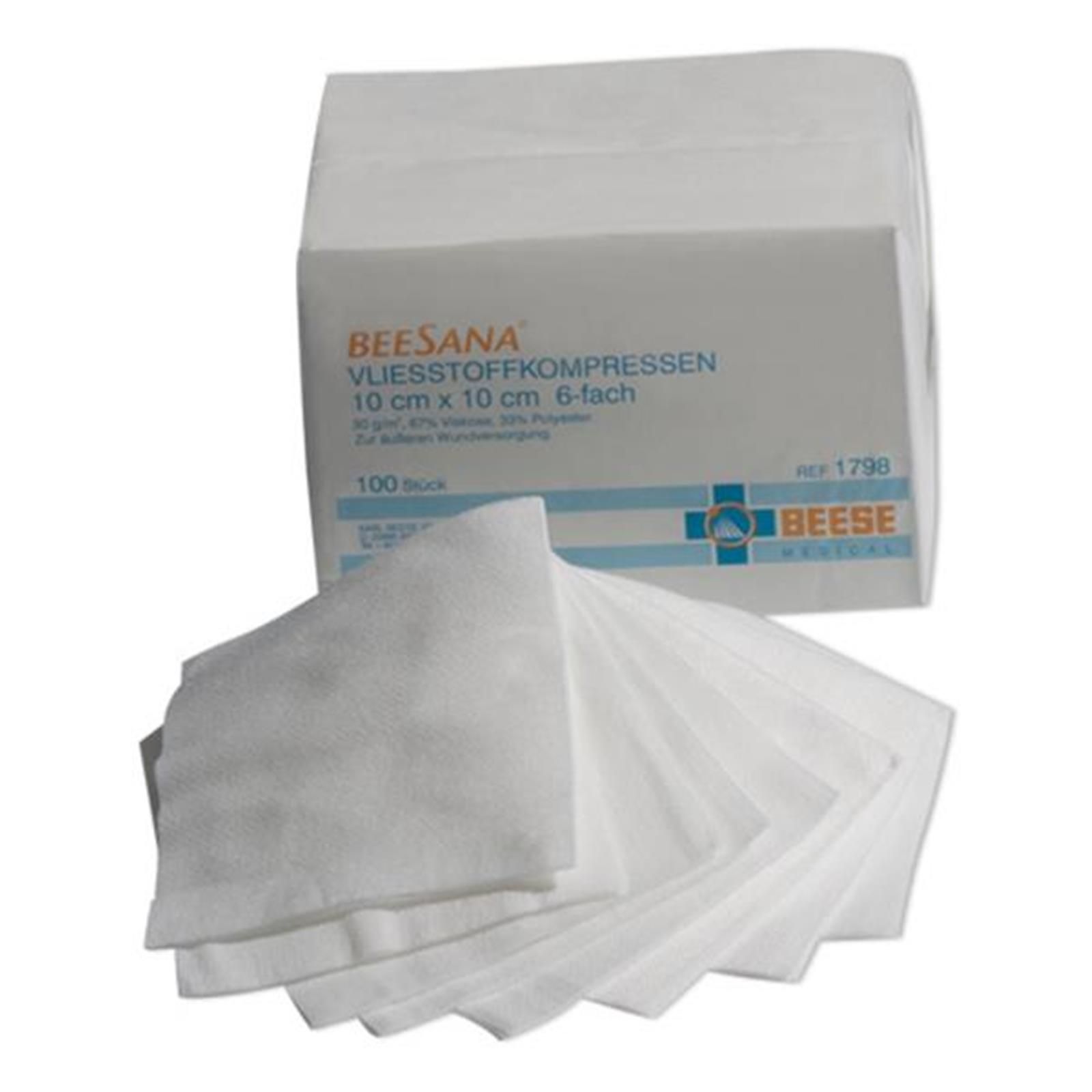Weiße Vliesstoffkompressen, 10 x 10 cm, 6-fach, aus der Verpackung entnommen. Verpackung mit Produktbezeichnung und Logo.