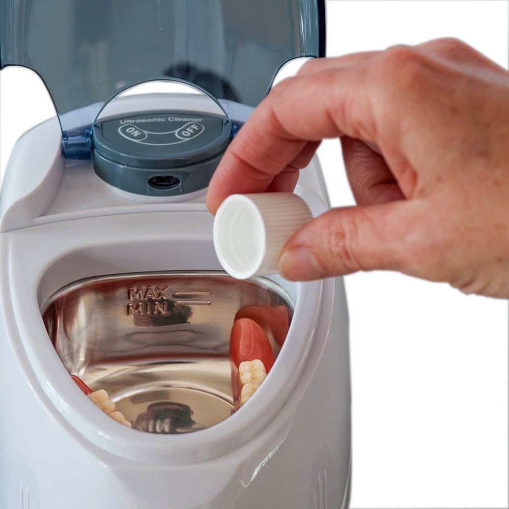 Ultraschallreiniger mit Prothese. Hand hält Deckel. Gerät mit Bedienfeld und Behälter für Reinigung.