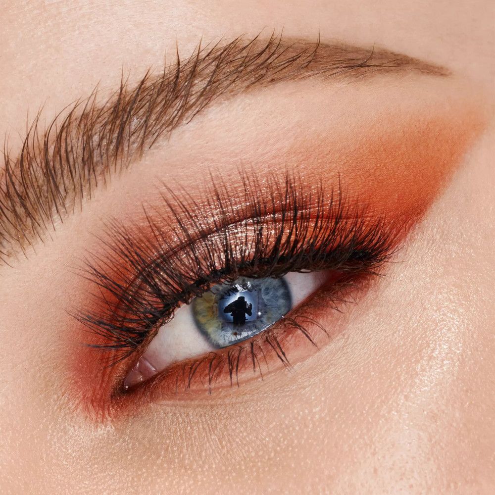 Nahaufnahme eines Auges mit geschminkten Augen. Wimpern und Lidschatten in Orange-Tönen.