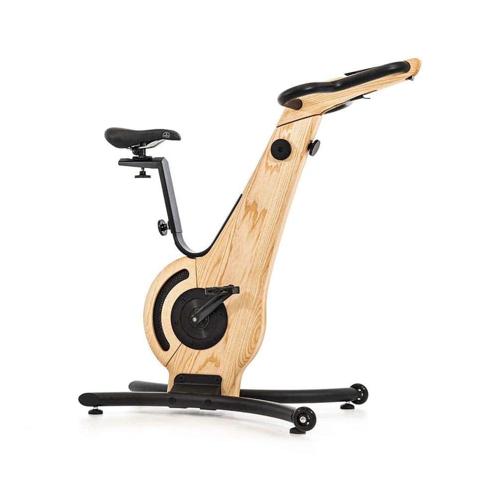 Hometrainer aus Holz. Schwarzer Sattel, Lenker und Pedale. Holzrahmen mit schwarzem Sockel. NOHrD-Logo auf dem Sattel.