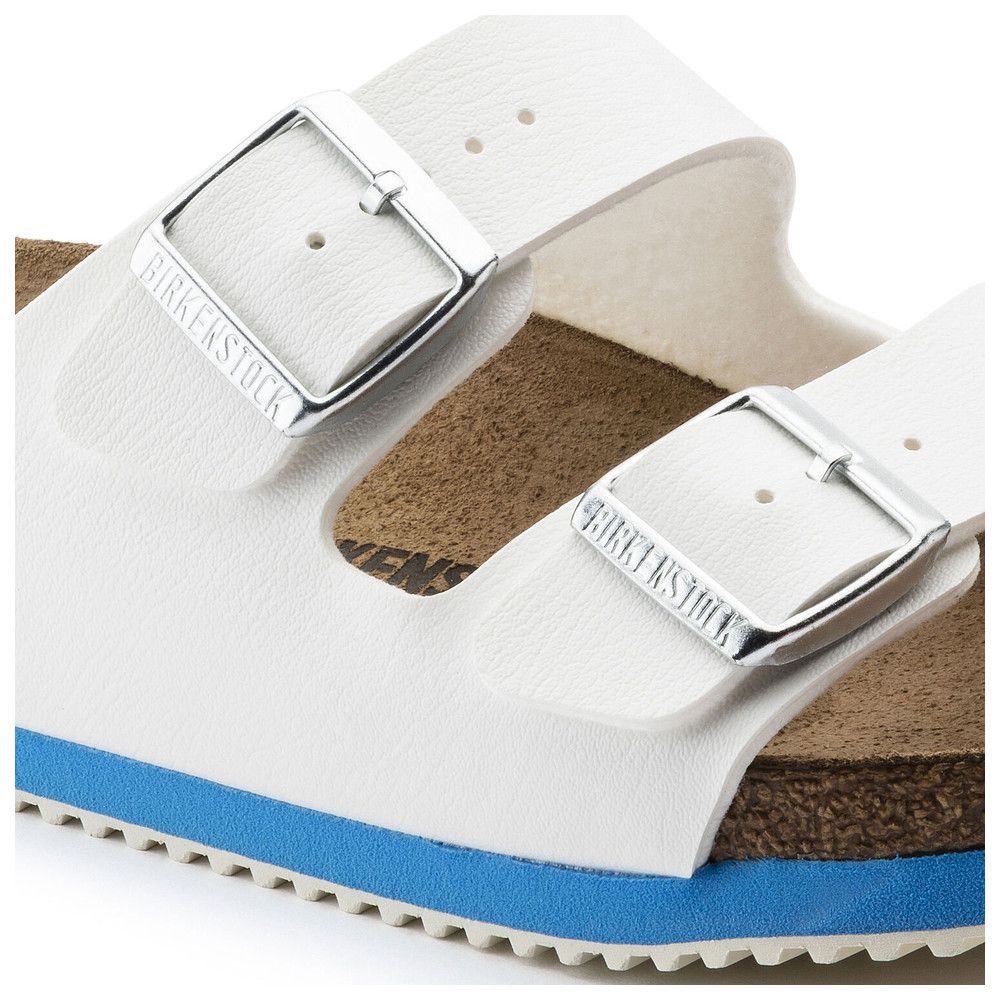Nahaufnahme einer weißen Sandale mit zwei Riemen. Silberne Schnallen mit Birkenstock-Logo. Blaue Sohlenkante.