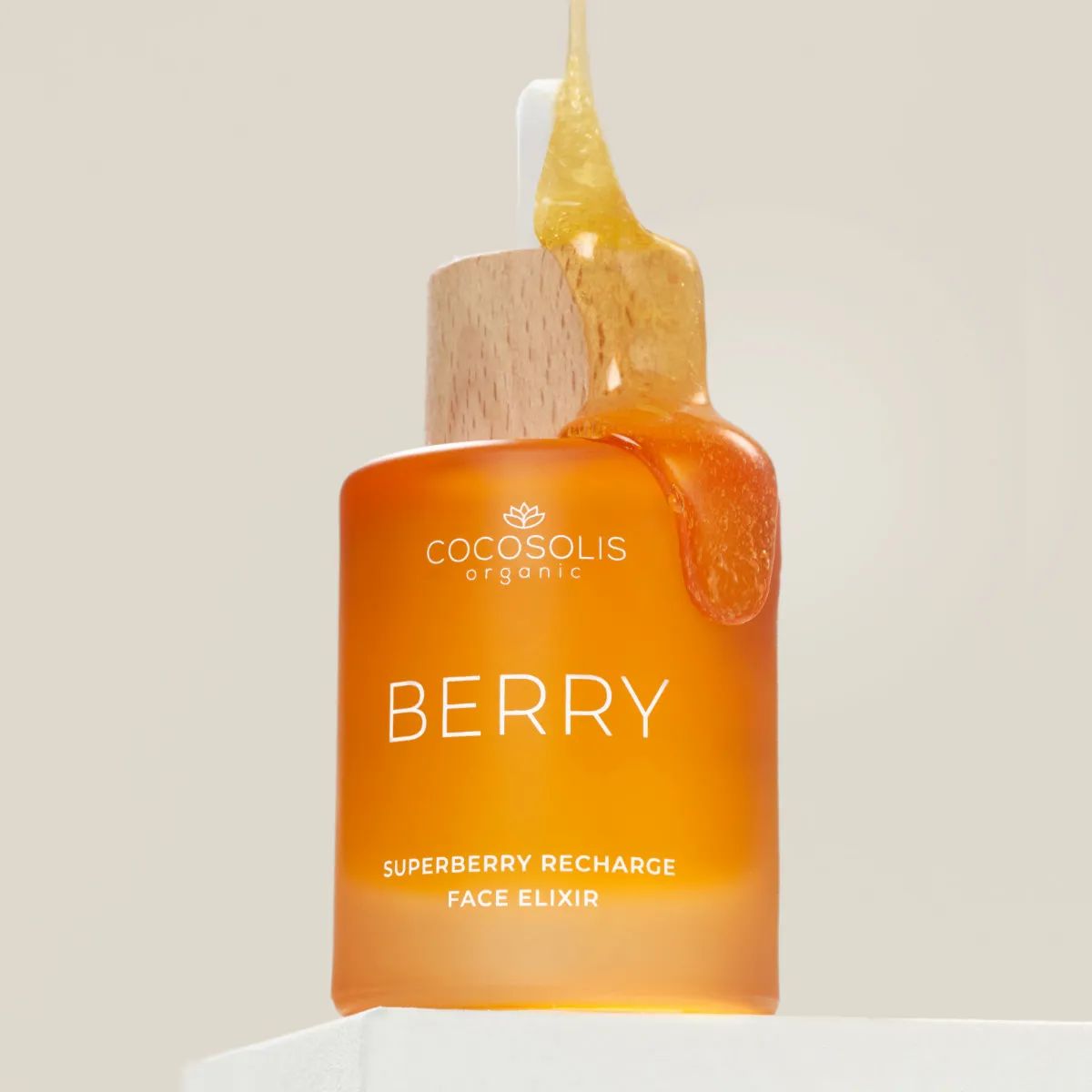 Orangefarbene Glasflasche mit Pipette, aus der goldenes Elixier auf den Flaschenhals tropft. Beschriftung: Cocosolis, Berry, Superberry Recharge Face Elixir.