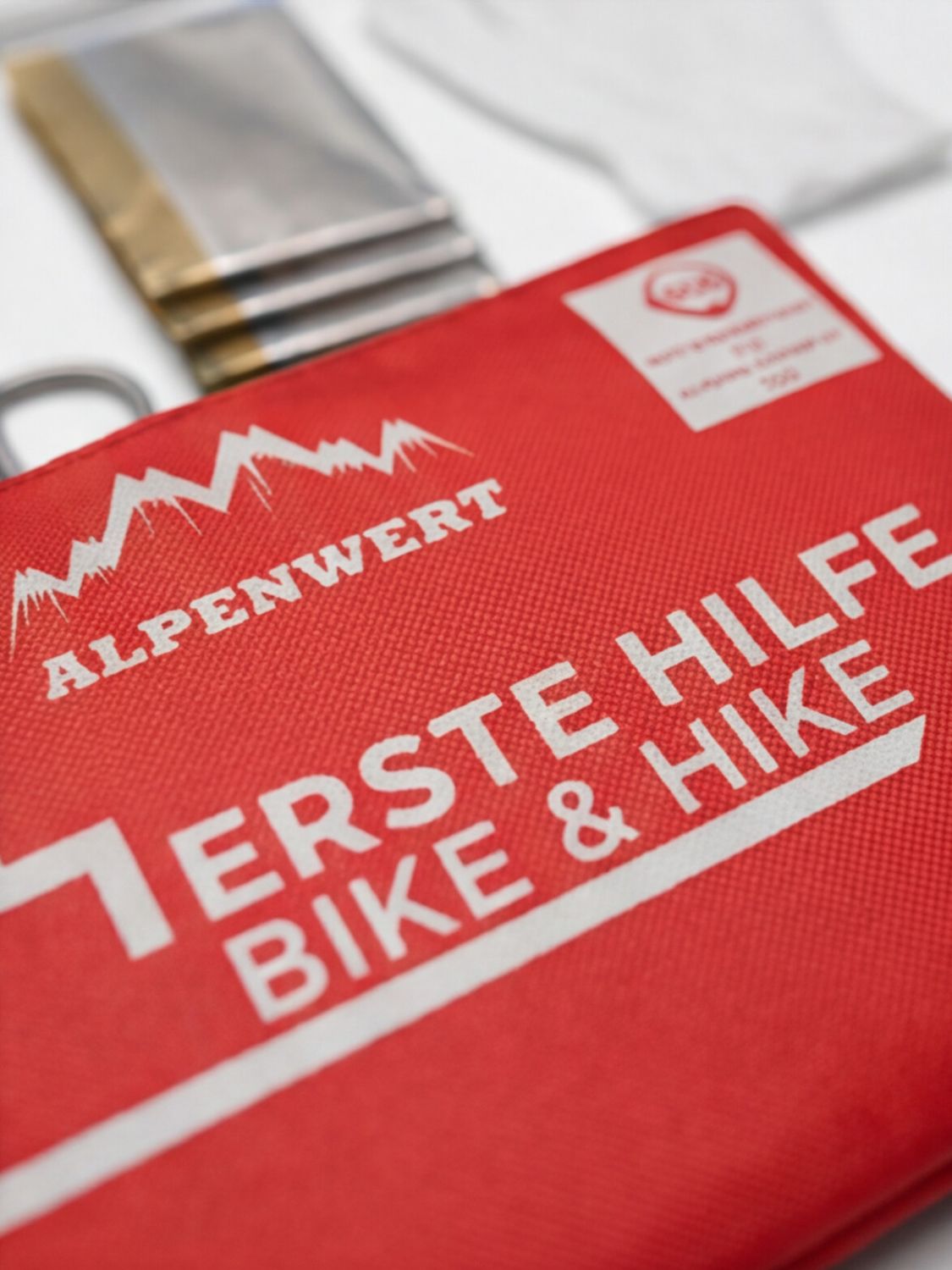 Nahaufnahme einer roten Erste-Hilfe-Tasche mit Alpenwert Logo und 'ERSTE HILFE BIKE & HIKE' Aufschrift.