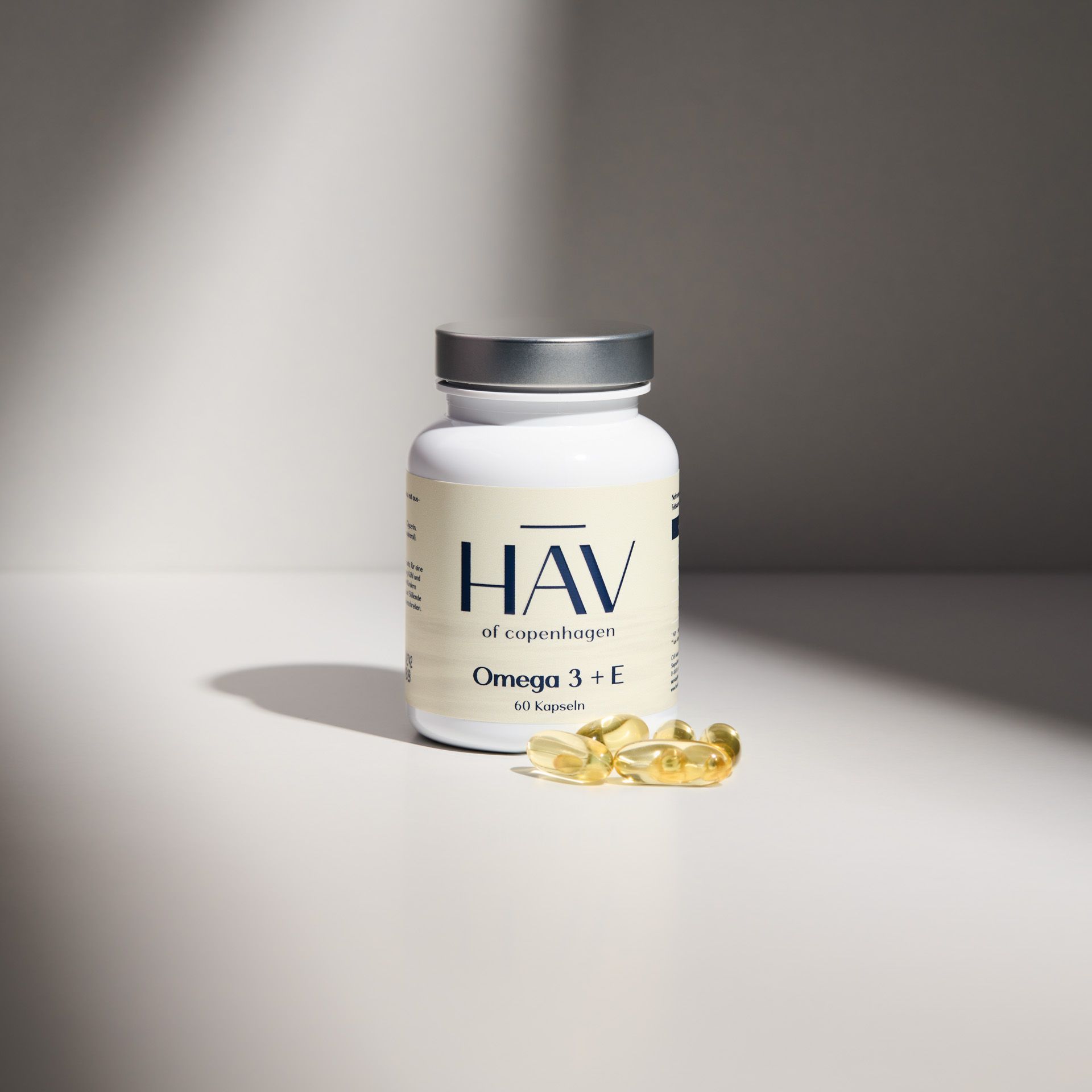Weiße Flasche HAV Omega 3 + E, 60 Kapseln. Einige Kapseln daneben. Silberner Deckel.