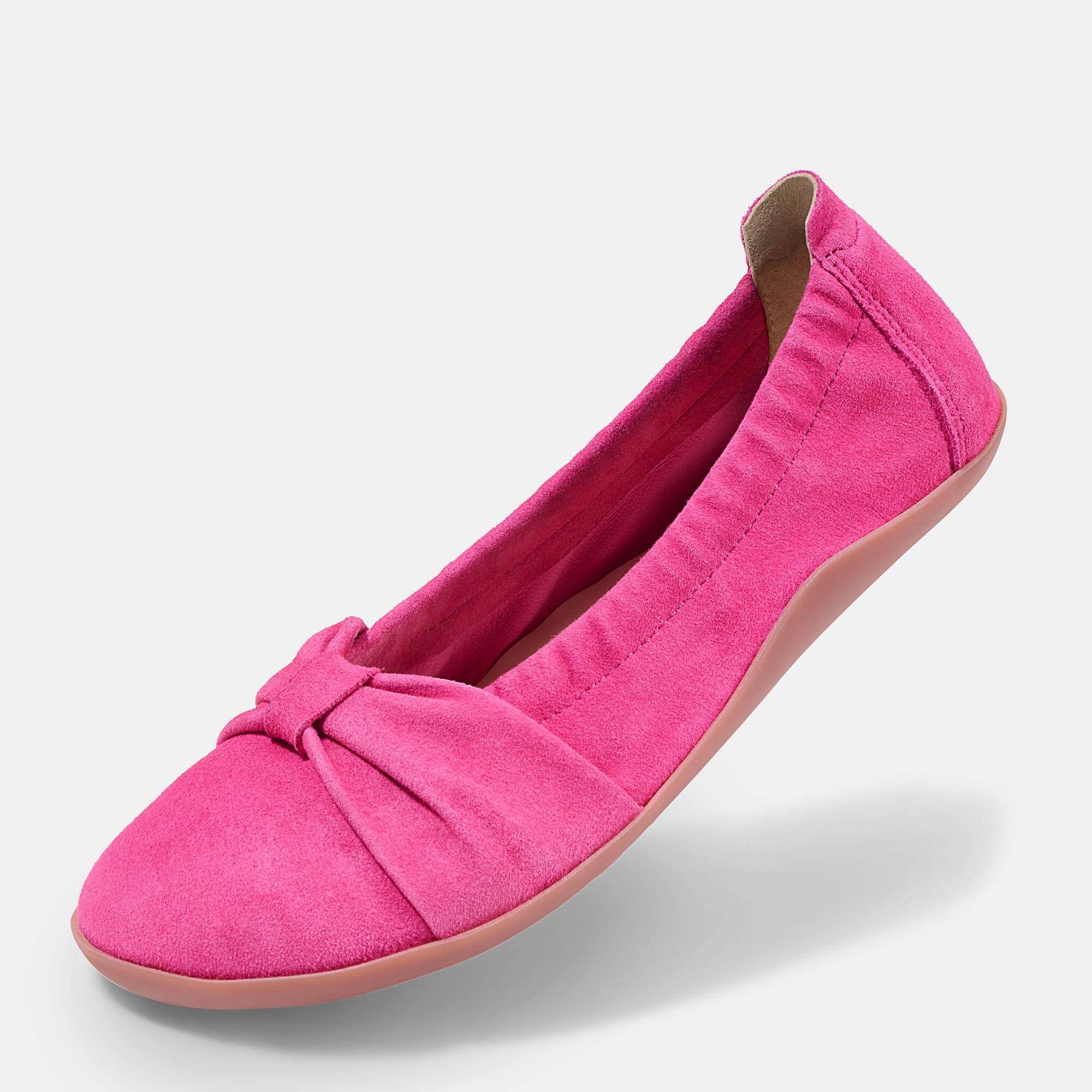 Eine pinke Ballerina aus Wildleder mit Schleifen-Detail und Gummizug, schräg von vorne.