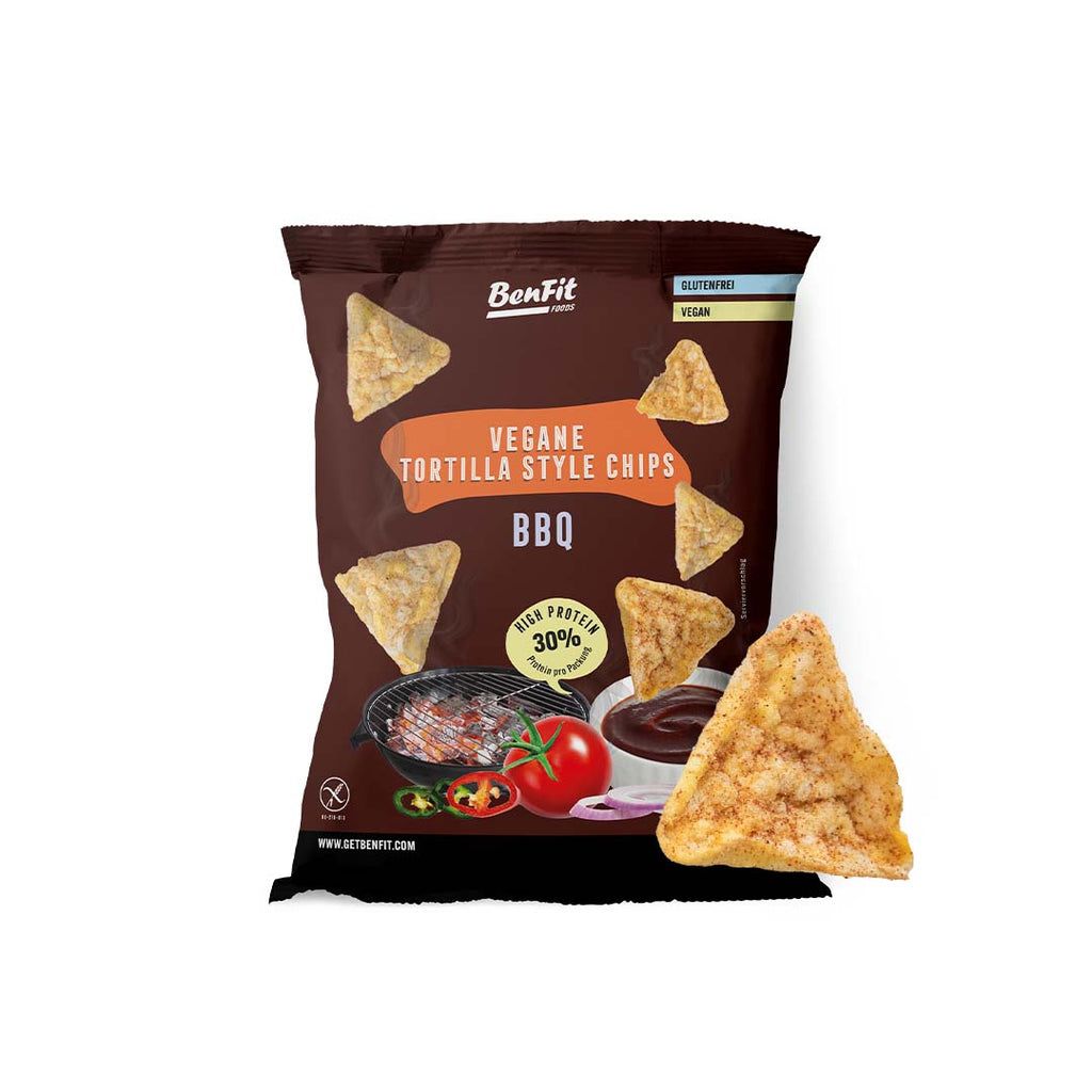 Braune Tüte mit veganen Tortilla-Chips BBQ. Aufschrift: High Protein 30%. Glutenfrei und vegan. Einzelner Chip rechts unten.