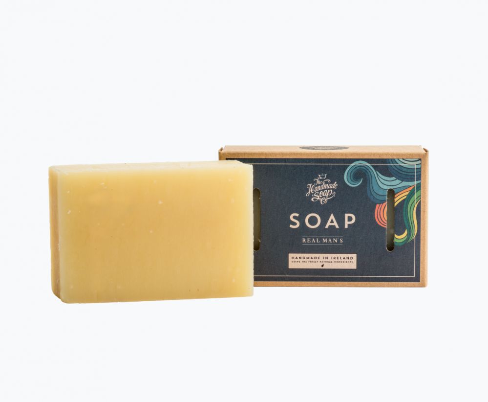 Rechteckige Seife, hellgelb. Daneben eine Schachtel mit der Aufschrift "SOAP REAL MAN'S" und dem Logo.