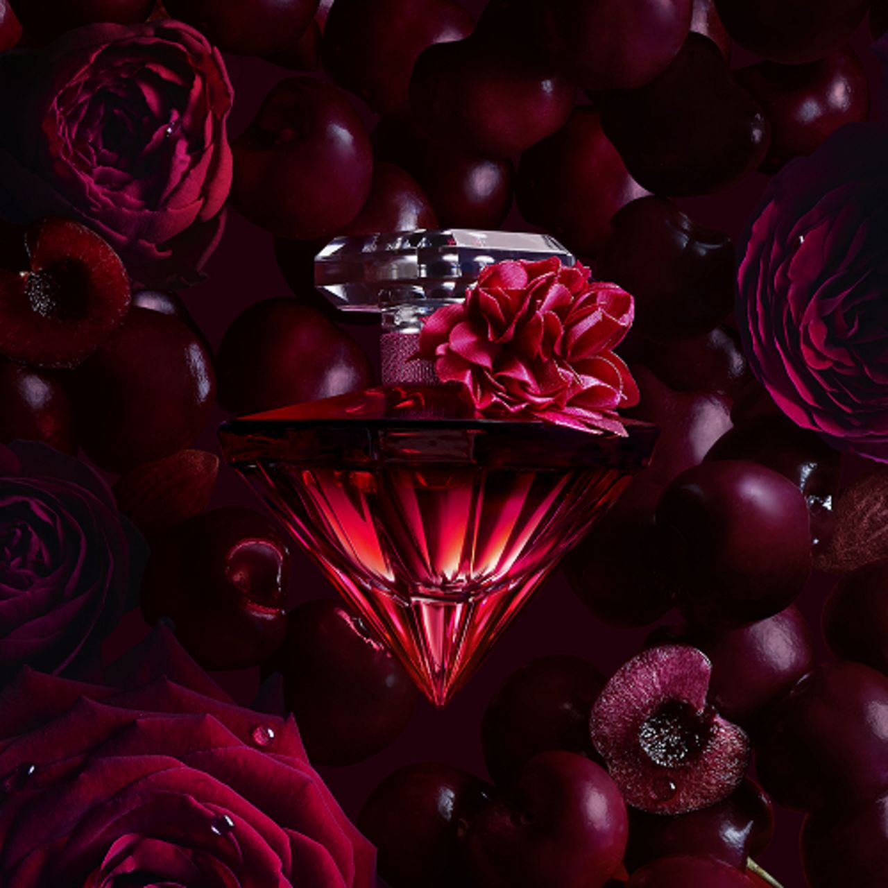 Roter Flakon in Diamantform mit Blüte, umgeben von Kirschen und Rosen. Lancôme Trésor La Nuit Intense E.d.P. Nat. Spray.