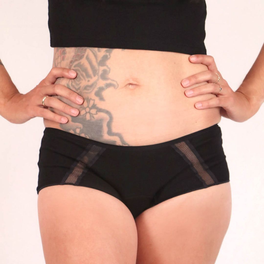 Schwarze Culotte mit Mesh-Einsätzen. Person vor weißem Hintergrund.