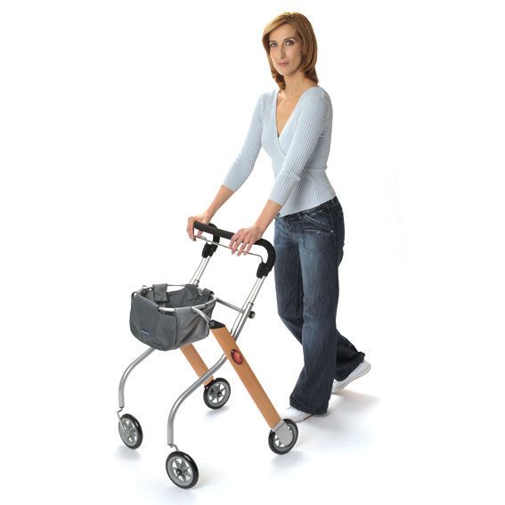 Frau mit Rollator mit Holzoptik-Rahmen, silbernen Metallbeinen, vier Rädern und Einkaufskorb.