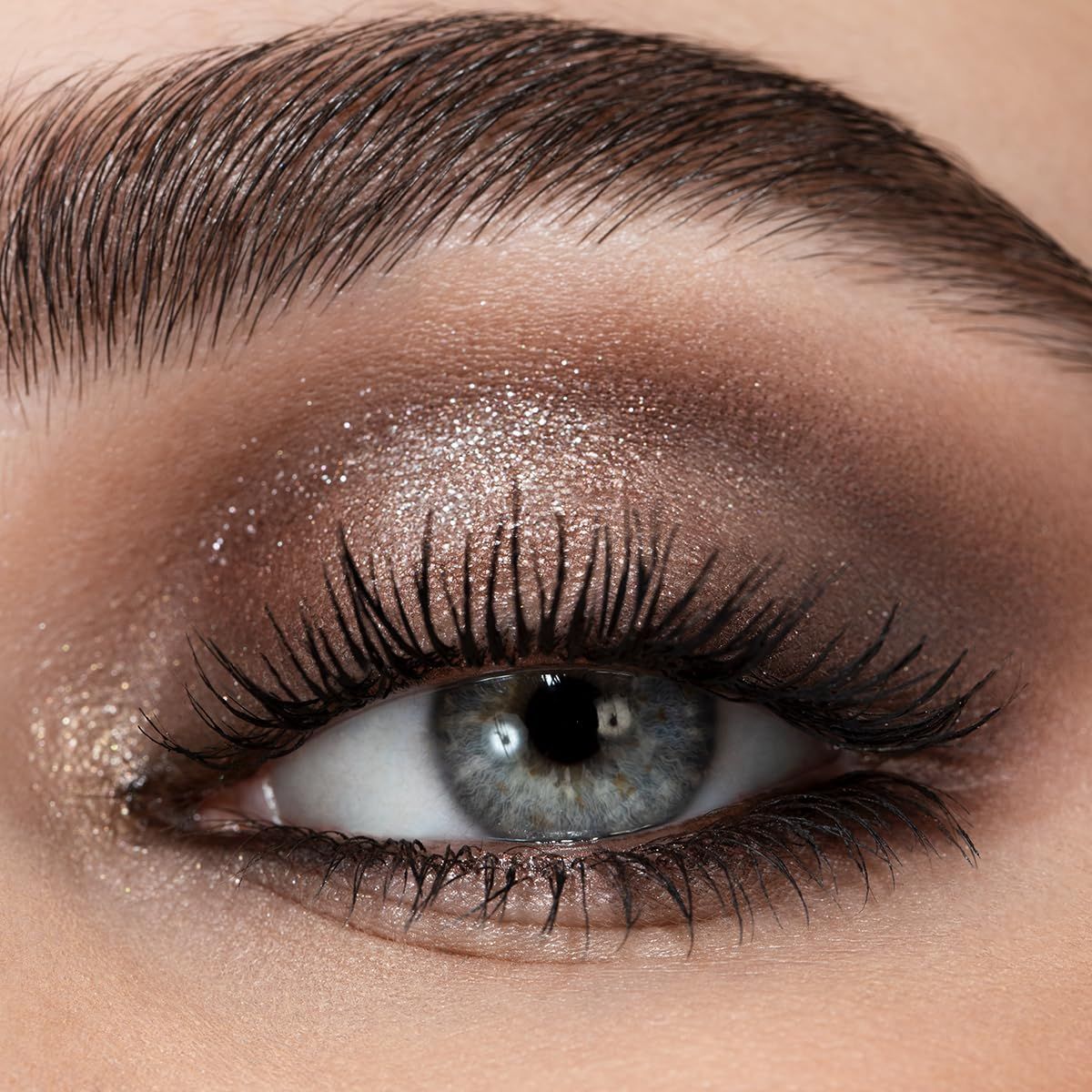 Ein Auge mit braunem und glitzerndem Lidschatten, Mascara und definierten Brauen.