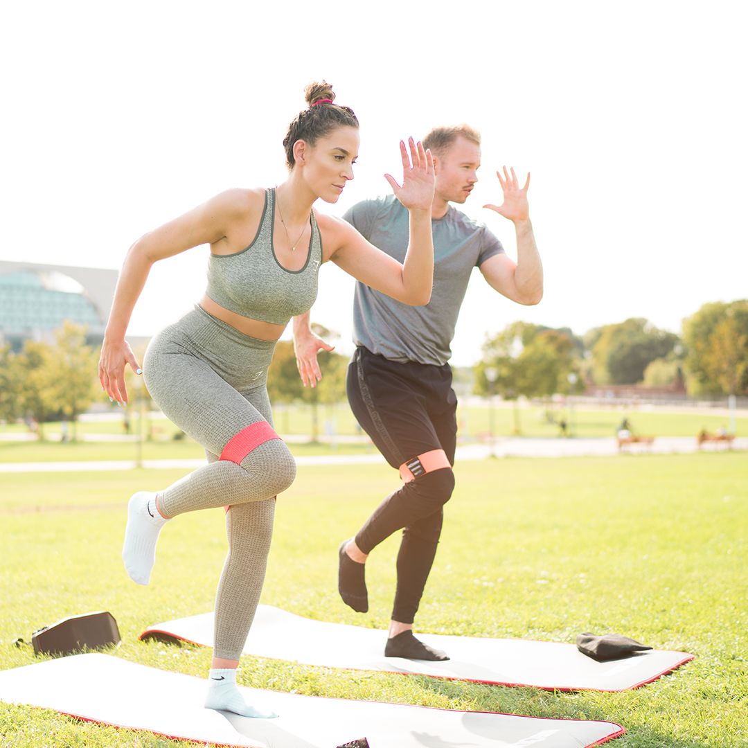 Zwei Personen trainieren im Freien mit Stoff-Fitnessbändern. Auf Matten.