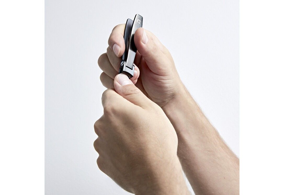 Hände halten einen schwarzen Nagelknipser. Der Knipser wird geöffnet. Weißer Hintergrund.