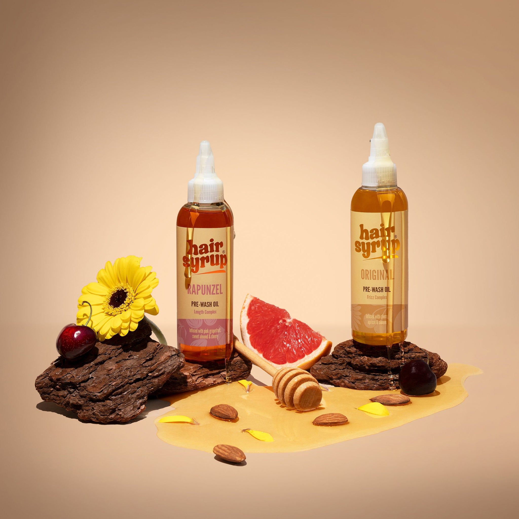 Zwei Flaschen Hair Syrup, eine mit dem Etikett 'Original', die andere mit 'Rapunzel'. Auf Holzstücken mit Grapefruit und Honig.