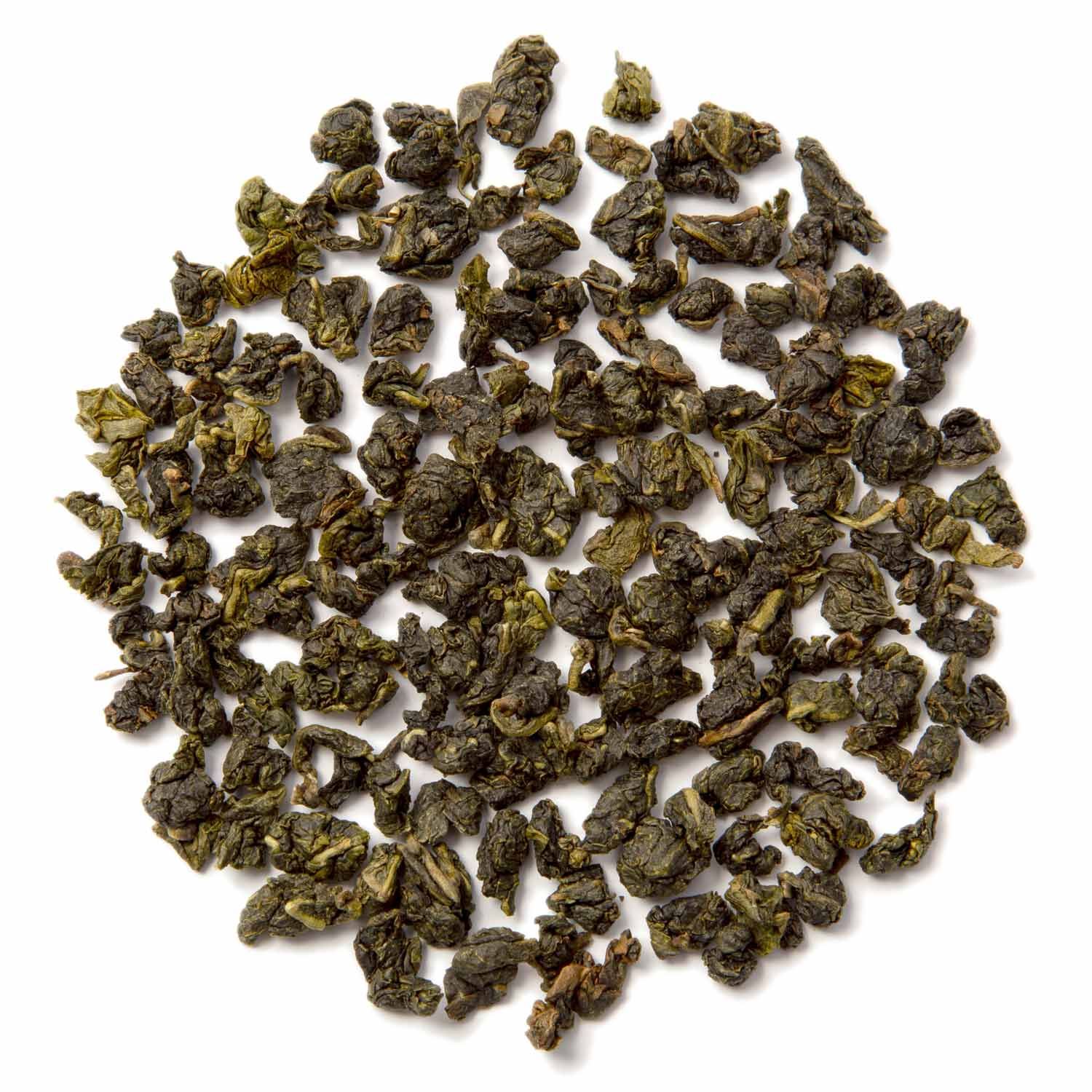 Haufen getrockneter, grüner Teeblätter auf weißem Hintergrund.