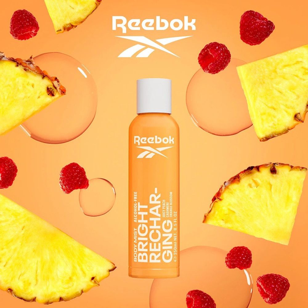 Orangefarbene Flasche mit weißem Deckel. Text: Reebok, Bright Recharging. Umgeben von Ananasstücken und Himbeeren.