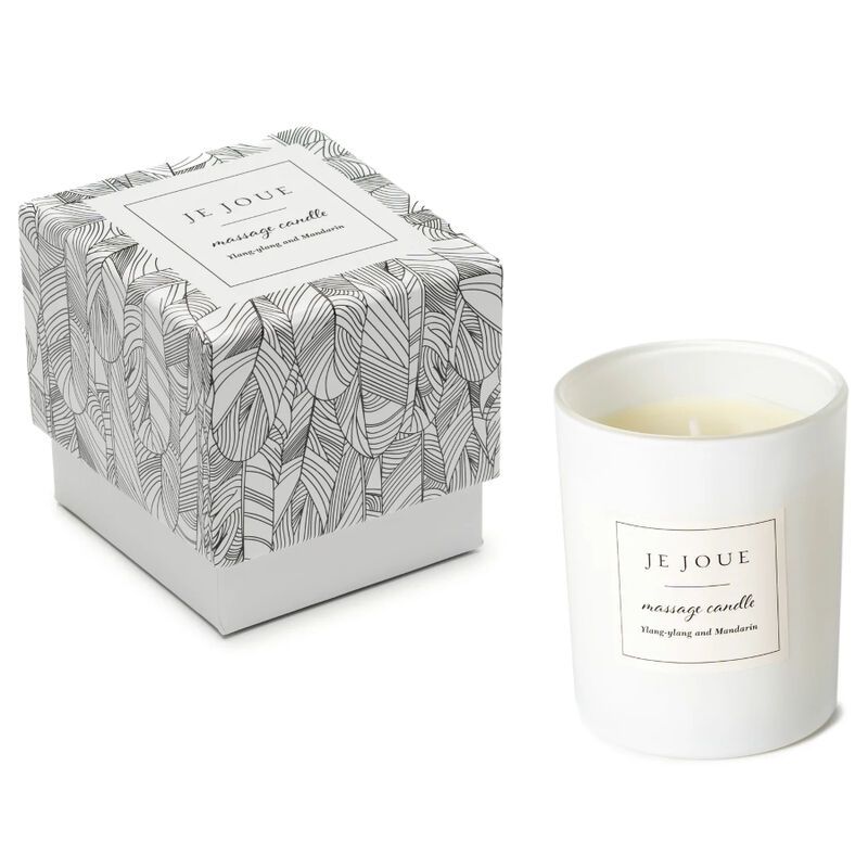 Kerze in weißem Becher neben Schachtel. Schachtel mit Federmuster, Aufkleber: JE JOUE, massage candle, Ylang ylang and Mandarin.