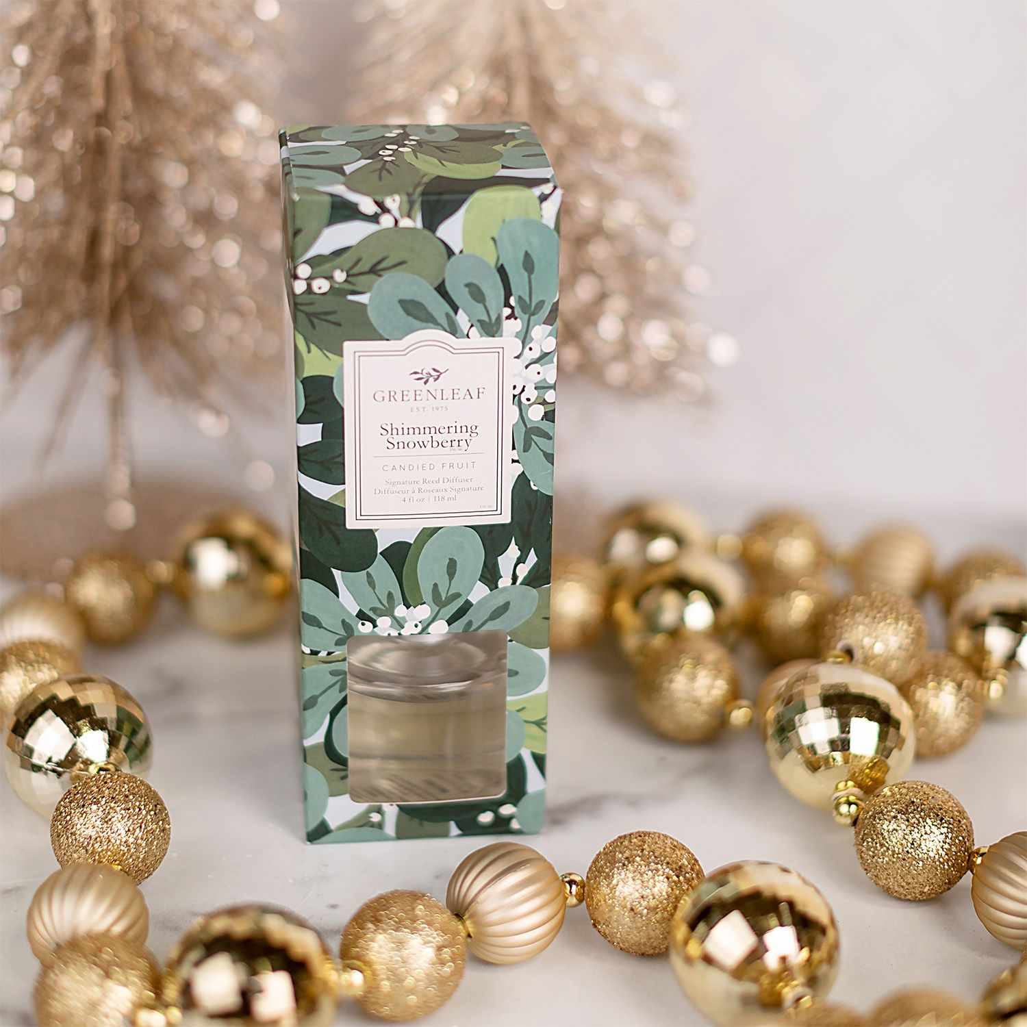 Glasflakon mit Duftstäbchen und Verpackung, umgeben von Weihnachtsdekoration.