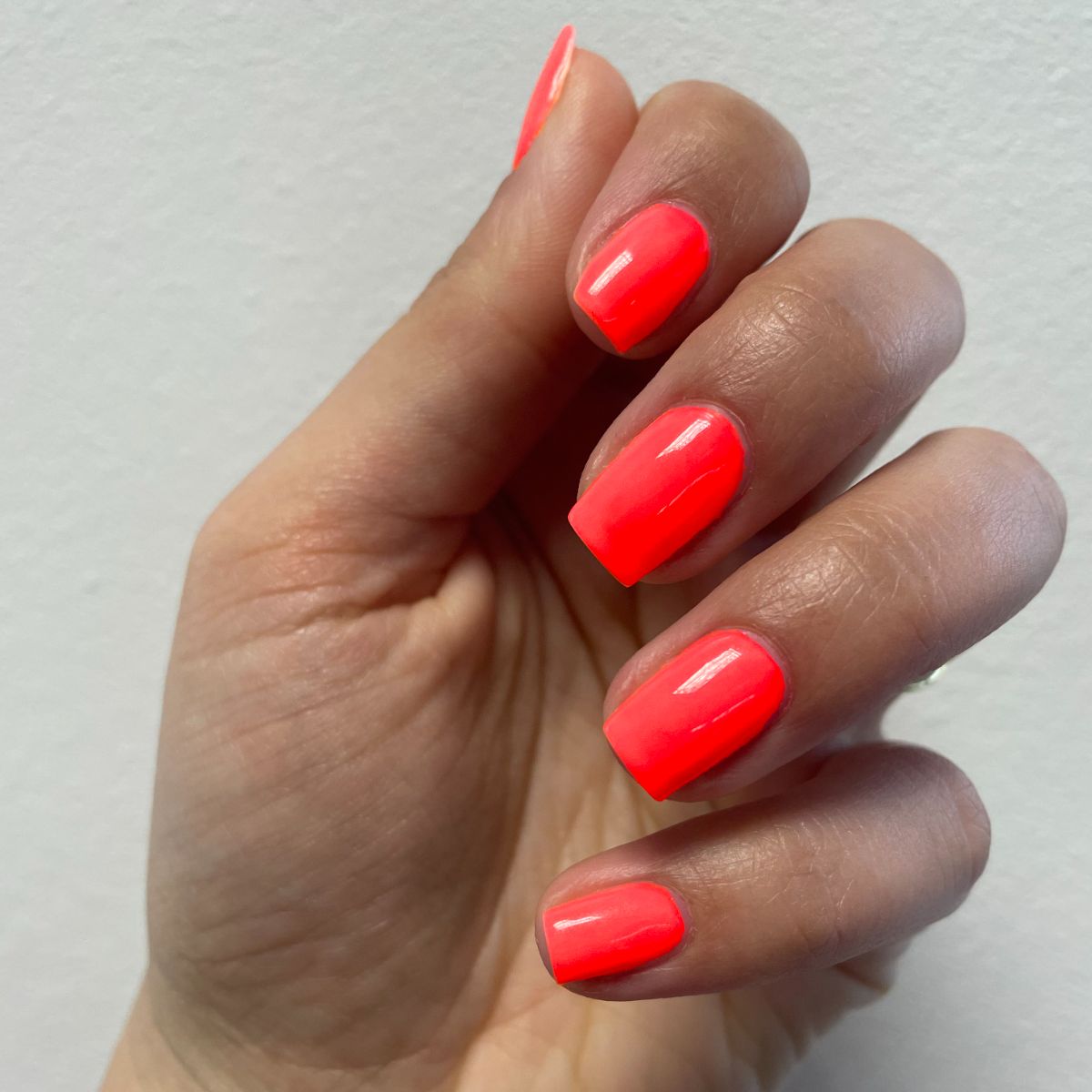 Hand mit neon-orangenen Nägeln. Die Nägel sind kurz und quadratisch gefeilt.