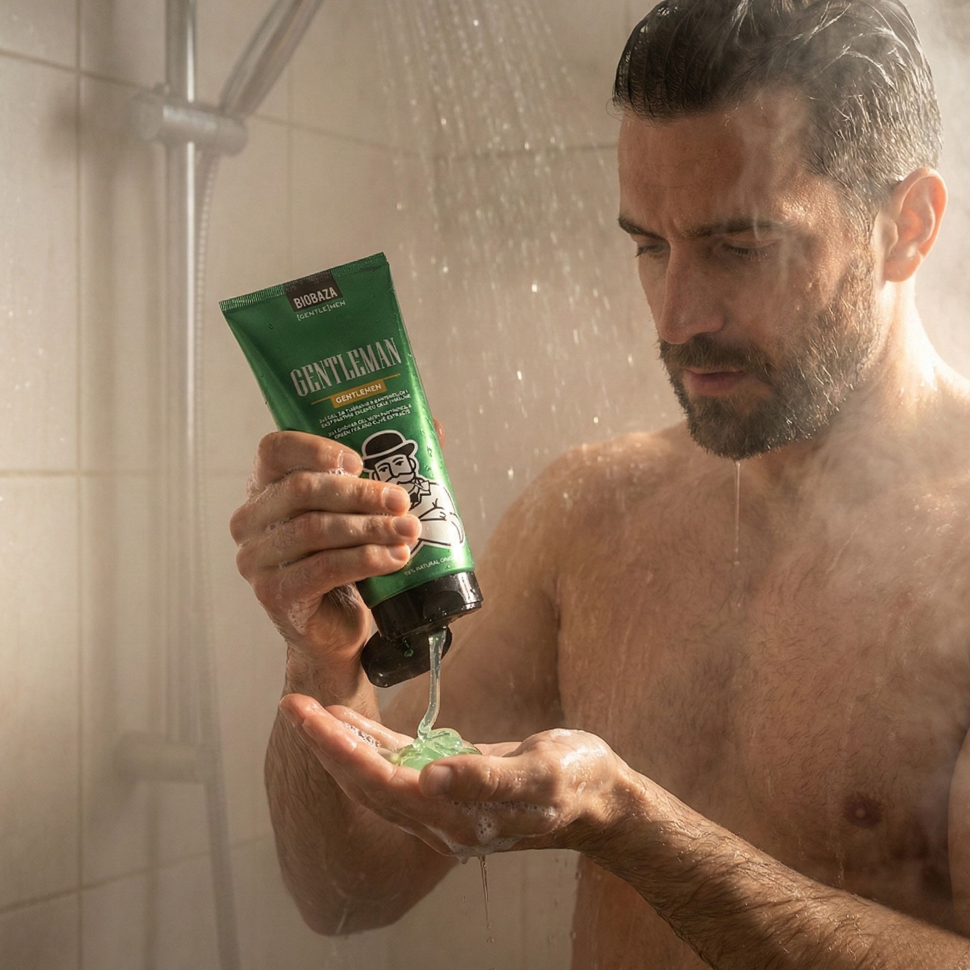 Mann in Dusche hält grüne Tube Duschgel "GENTLEMAN". Gel fließt in seine Hand.
