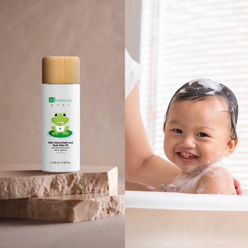 Dr. Botanicals Babyöl Flasche neben einem lächelnden Baby in der Badewanne.