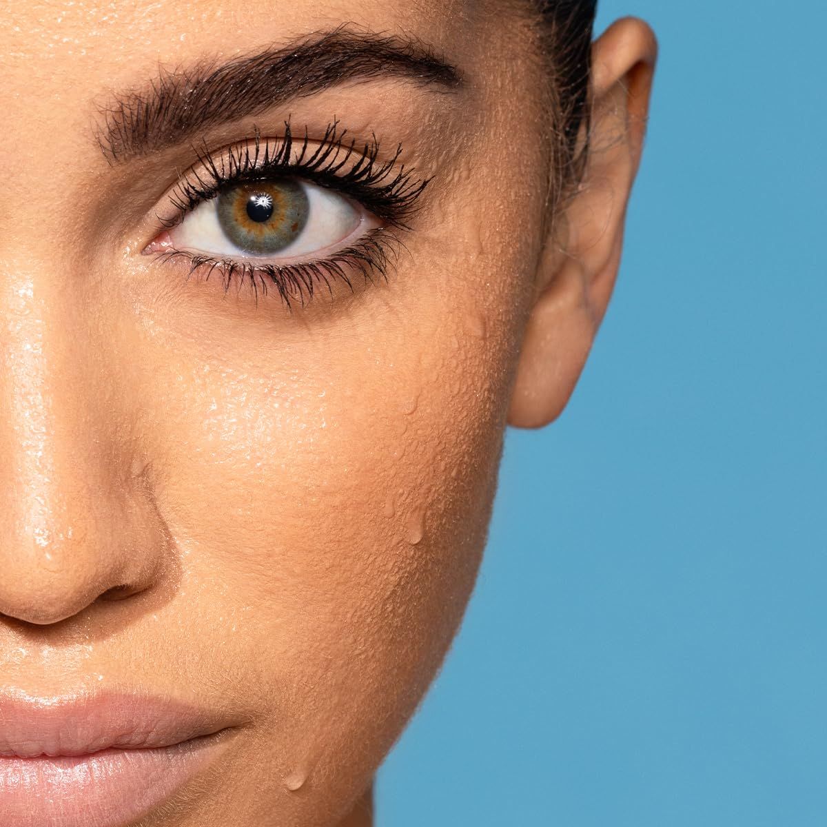 Nahaufnahme eines Gesichts mit Wassertropfen. Auge mit getuschten Wimpern. Blauer Hintergrund.