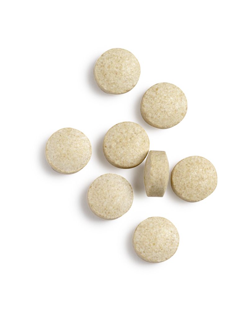 Sieben runde, beige Tabletten. Eine Tablette ist von der Seite sichtbar. Auf weißem Hintergrund.