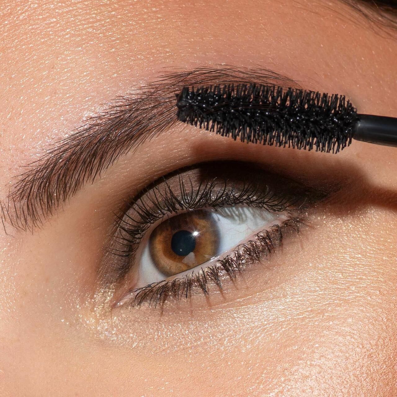 Auge mit Mascara-Applikator. Schwarze Mascara auf Wimpern. Produktname und Marke nicht sichtbar.