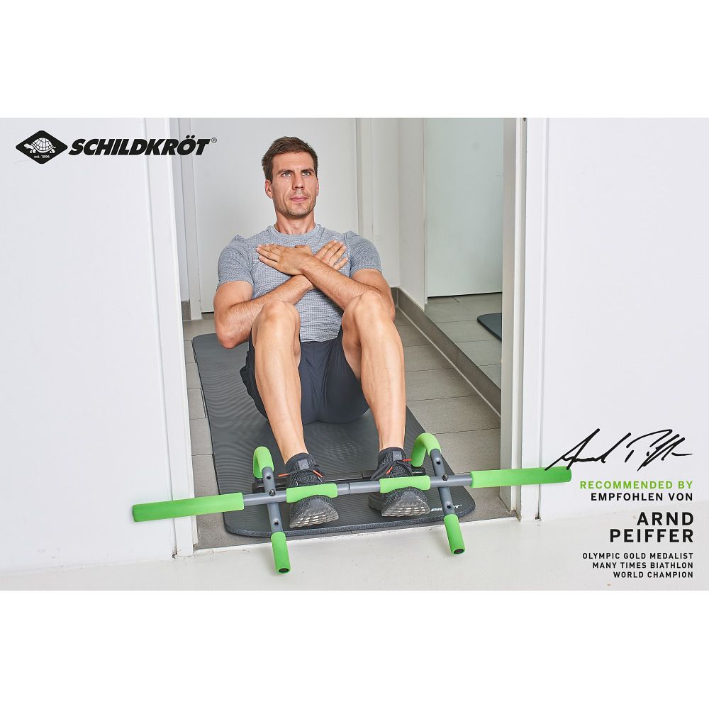 Mann sitzt vor dem Schildkröt Türreck Multifunktional 4 in 1. Das Gerät liegt auf einer Matte. Griffe grün.