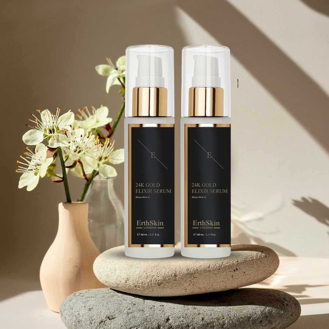 Zwei Serumflaschen mit goldenen Pumpköpfen und schwarzem Etikett. Aufschrift: 24K Gold Elixir Serum, ErthSkin London. Auf Steinen.