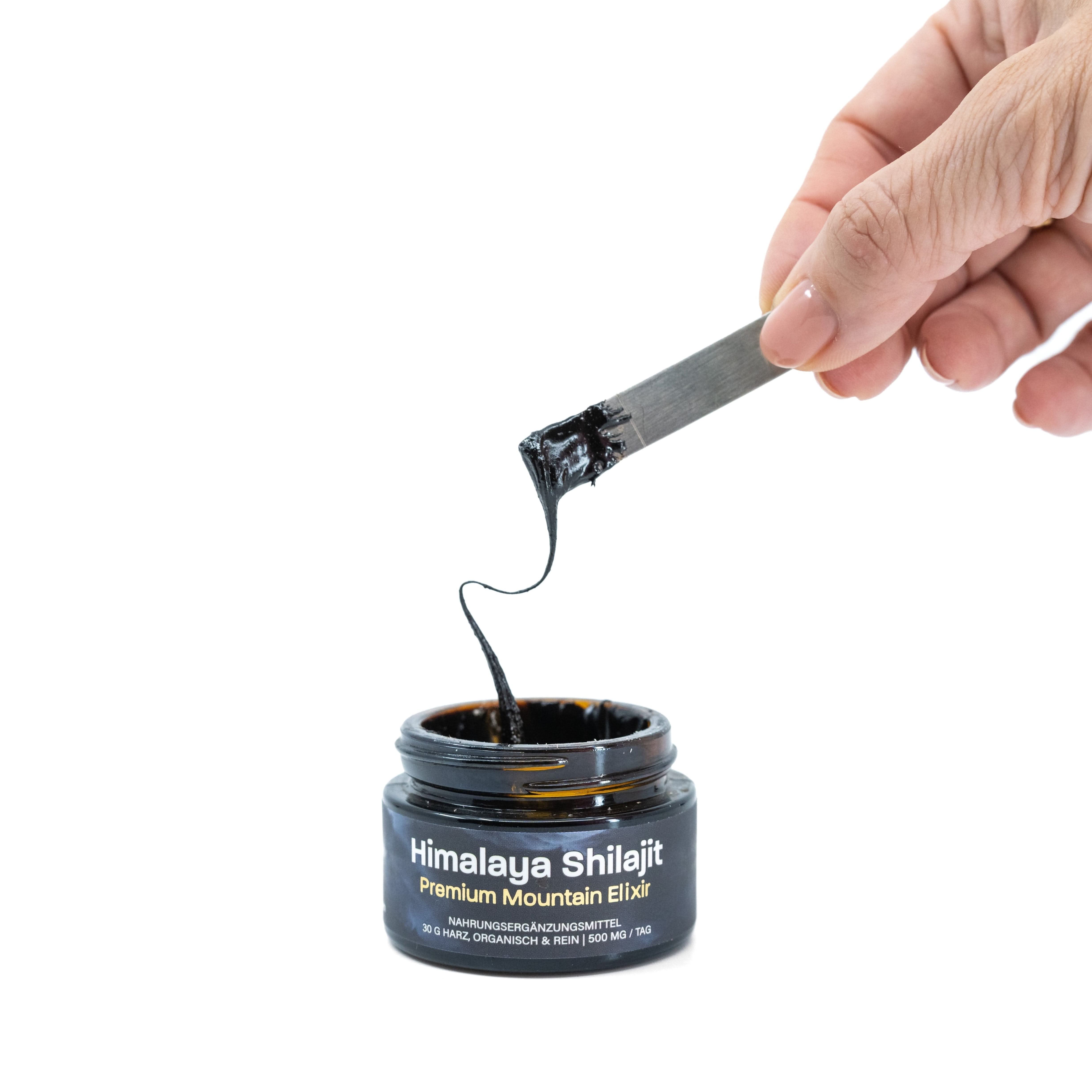 Dunkles, zähflüssiges Himalaya Shilajit wird mit einem Spatel aus einem Glasbehälter entnommen.