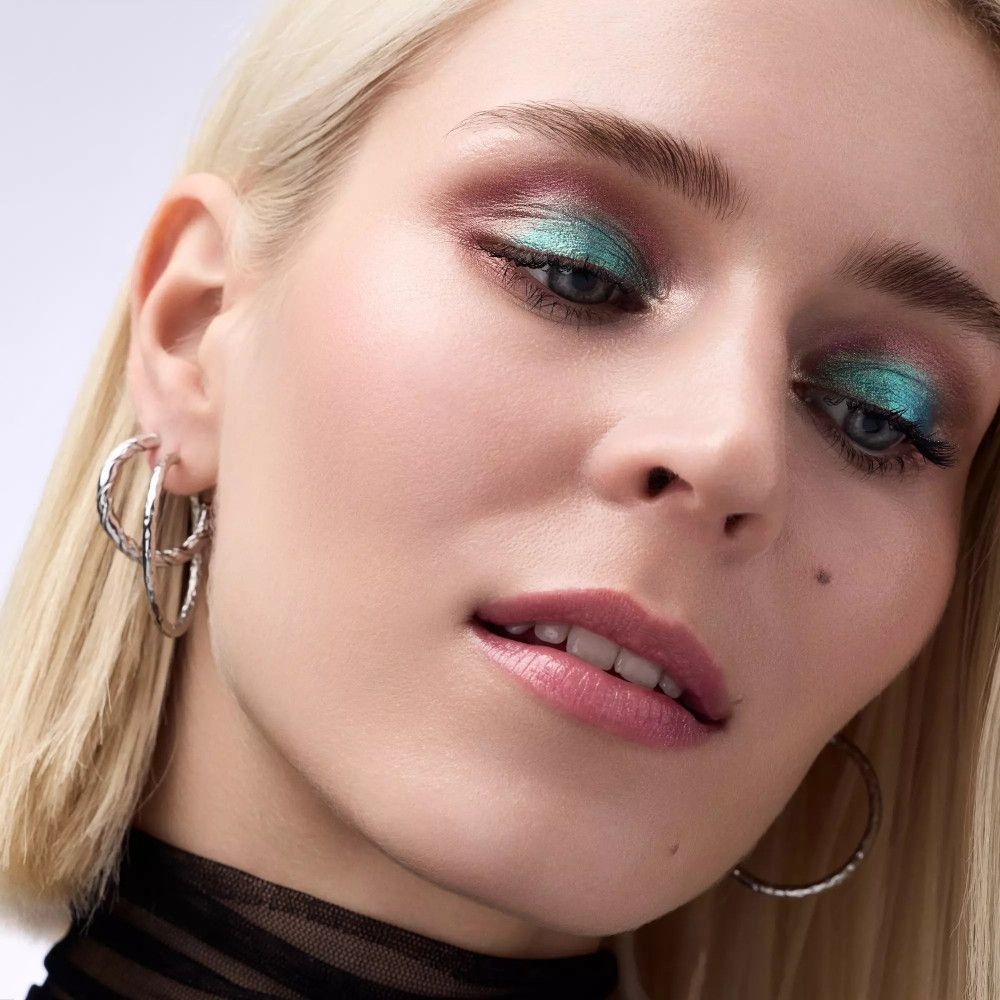 Porträt einer Frau mit grünem Lidschatten. Blonde Haare, silberne Ohrringe.