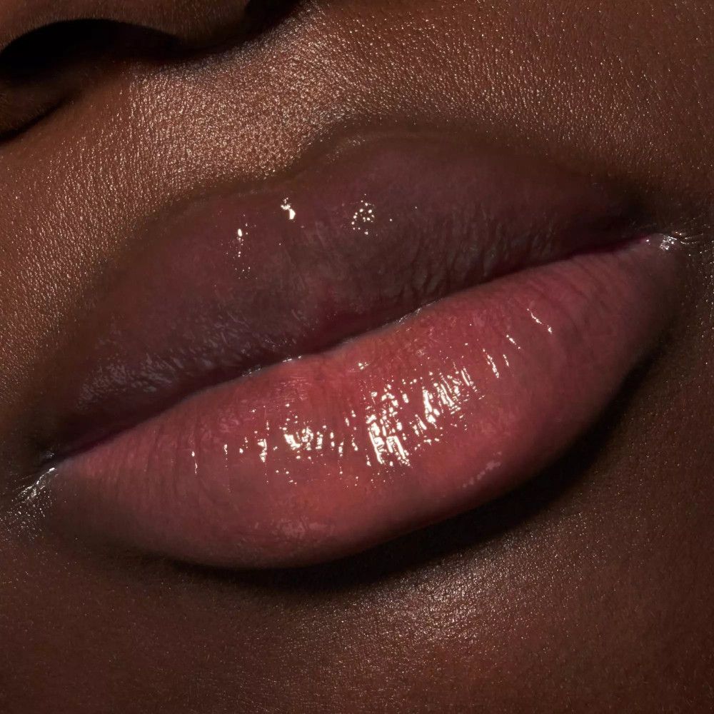 Nahaufnahme von Lippen. Glänzender, rosafarbener Lippenbalsam auf dunkler Haut.