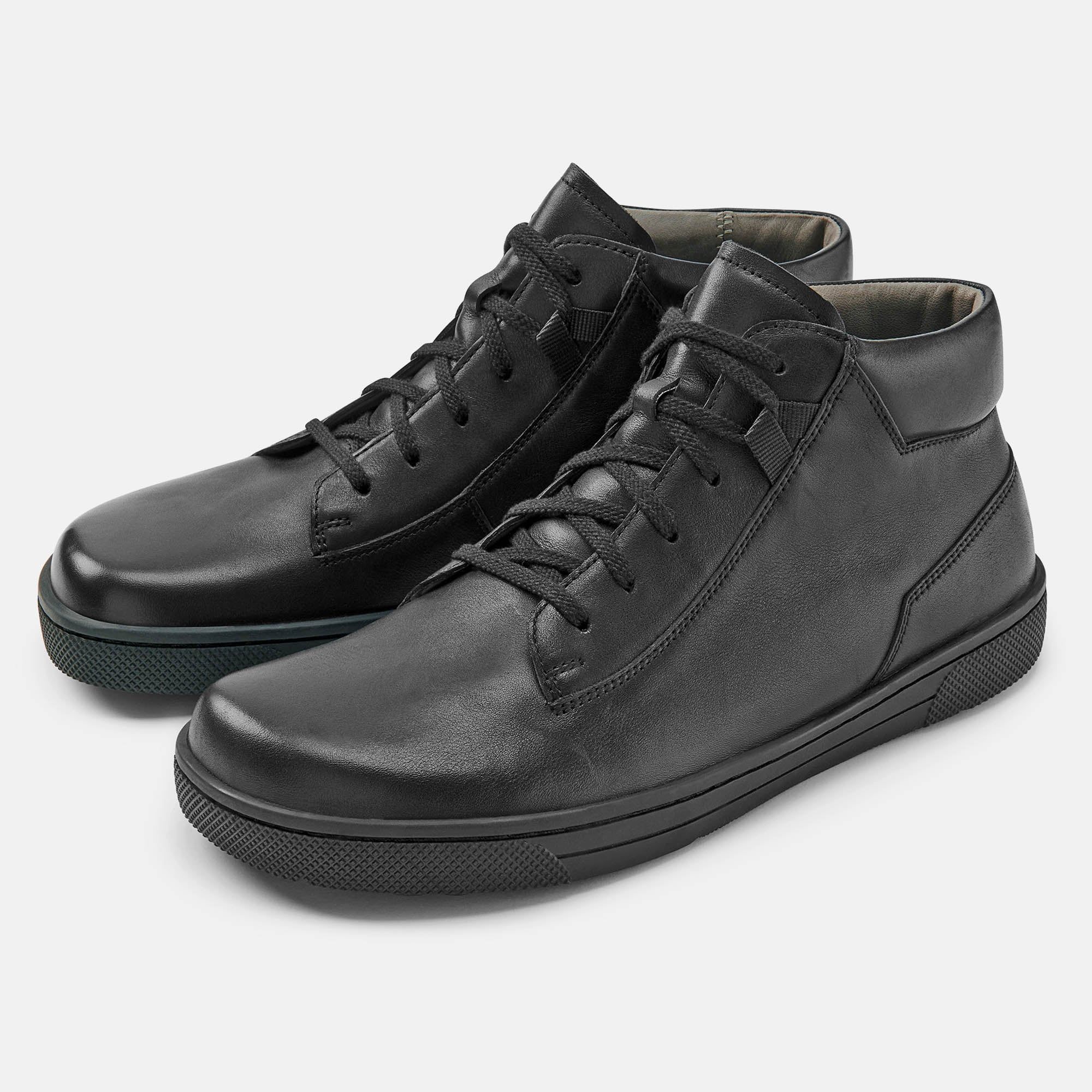 Schwarze Stiefeletten mit Schnürsenkeln. Flache Sohle, breite Passform. Zwei Schuhe nebeneinander.