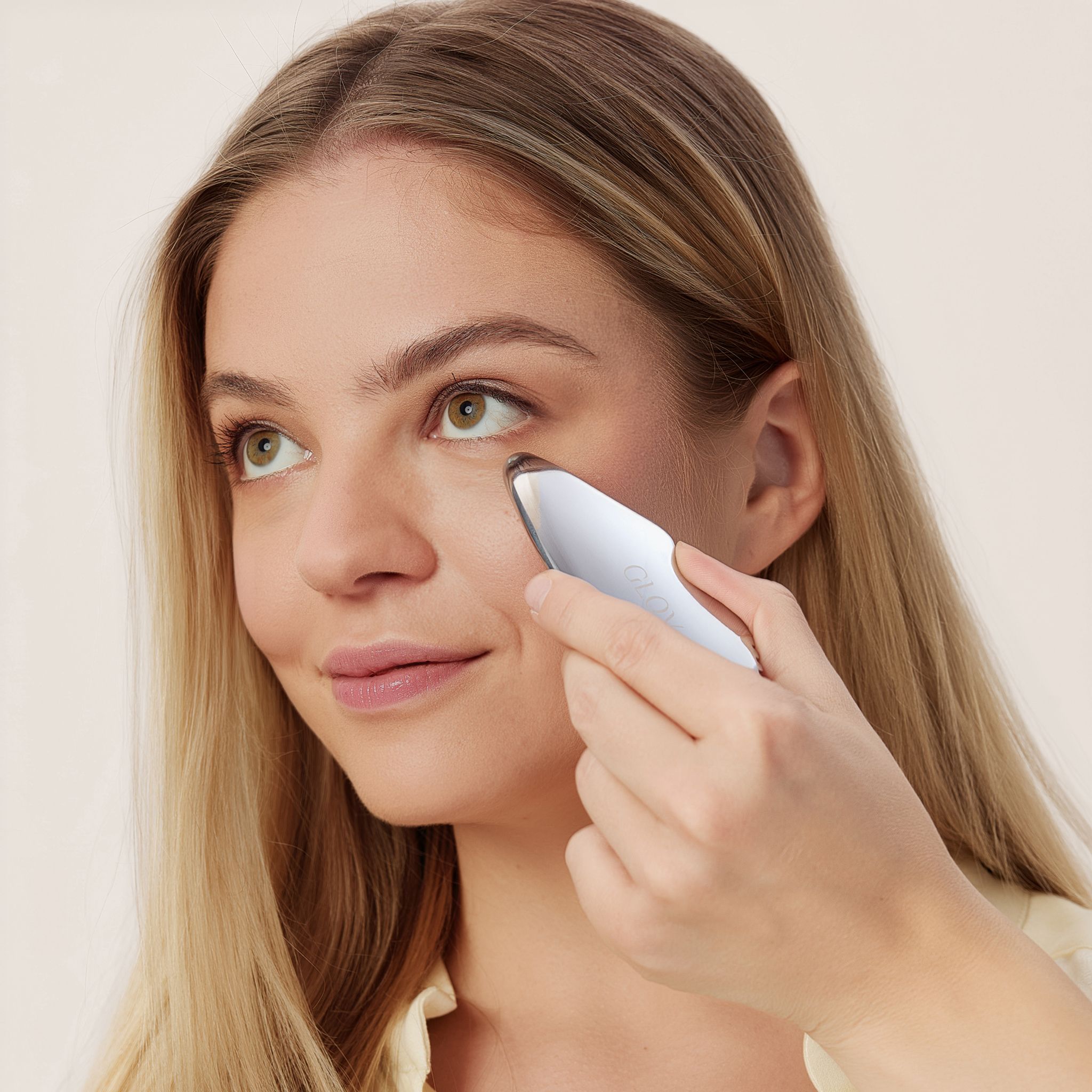 Eine Frau wendet ein weißes, ergonomisches Werkzeug unter ihrem Auge an.