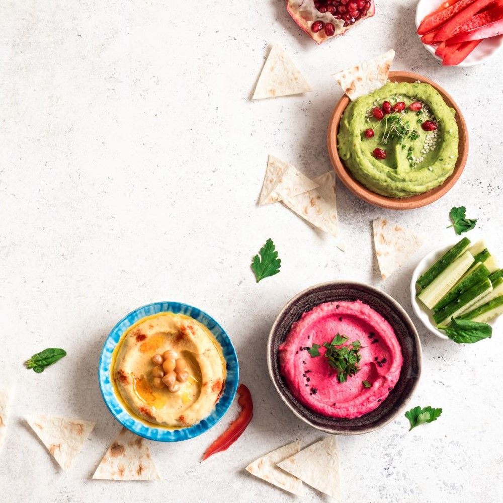 Verschiedene Dips in Schalen, mit Brot und Gemüse. Hummus, Avocado-Dip und Rote-Bete-Dip.