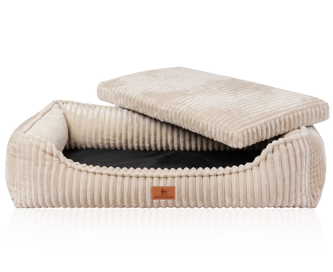 Beiges Hundebett aus Cord mit erhöhtem Rand, Kissen herausgenommen. Brauner Logo-Patch sichtbar.