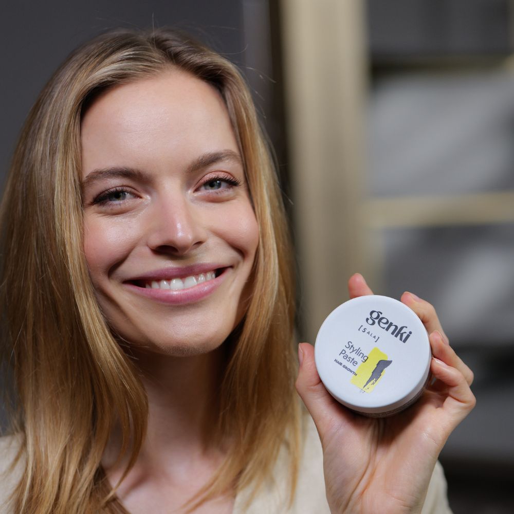 Frau hält Genki Styling Paste Dose. Grauer Deckel, schwarzer Schriftzug, gelber Farbfleck.