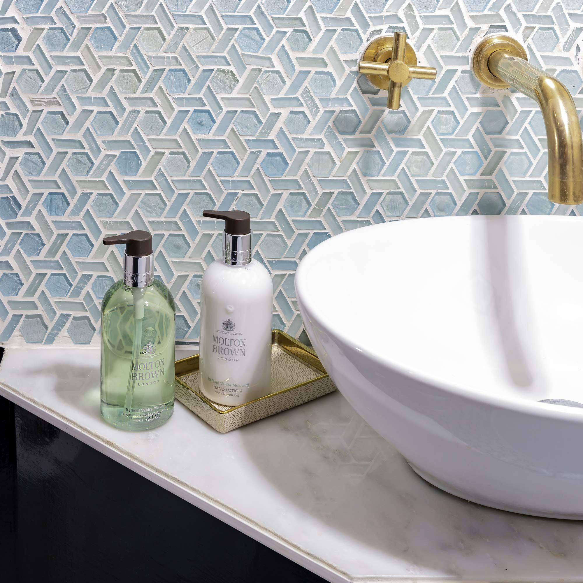 Zwei Flaschen Handlotion neben einem Waschbecken. Eine grüne und eine weiße Flasche mit Pumpe. Aufschrift: Molton Brown.